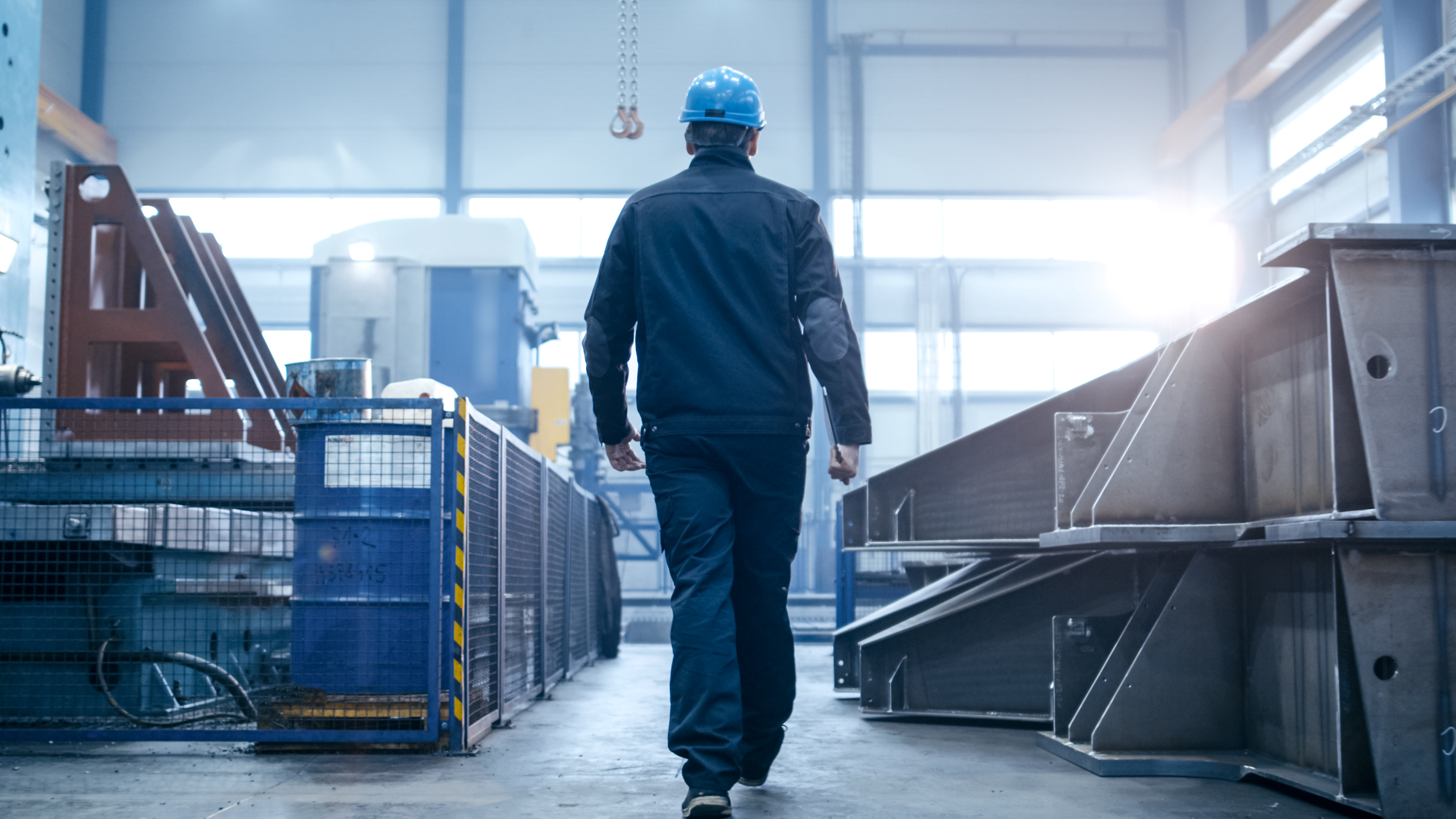 Factory worker in a hard hat is walking through industrial facil